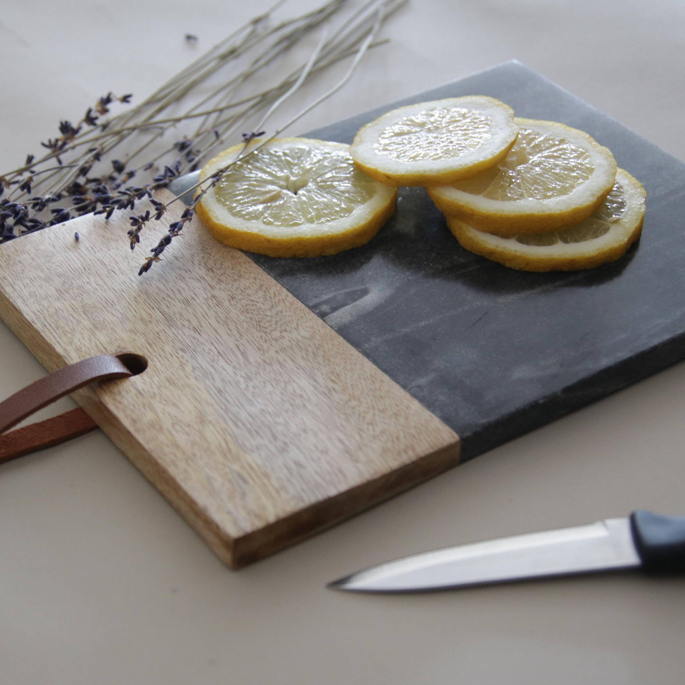 Sliced lemons on a wooden and slate cutting board with a knife and lavender flowers.