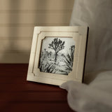 Framed artwork of a tree on a wooden surface with a blurred background