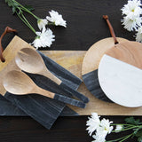 Wooden spoons and cutting boards on a dark surface with white flowers.
