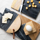 Wooden and marble cutting board with cheese, crackers, and an egg on a light gray surface.