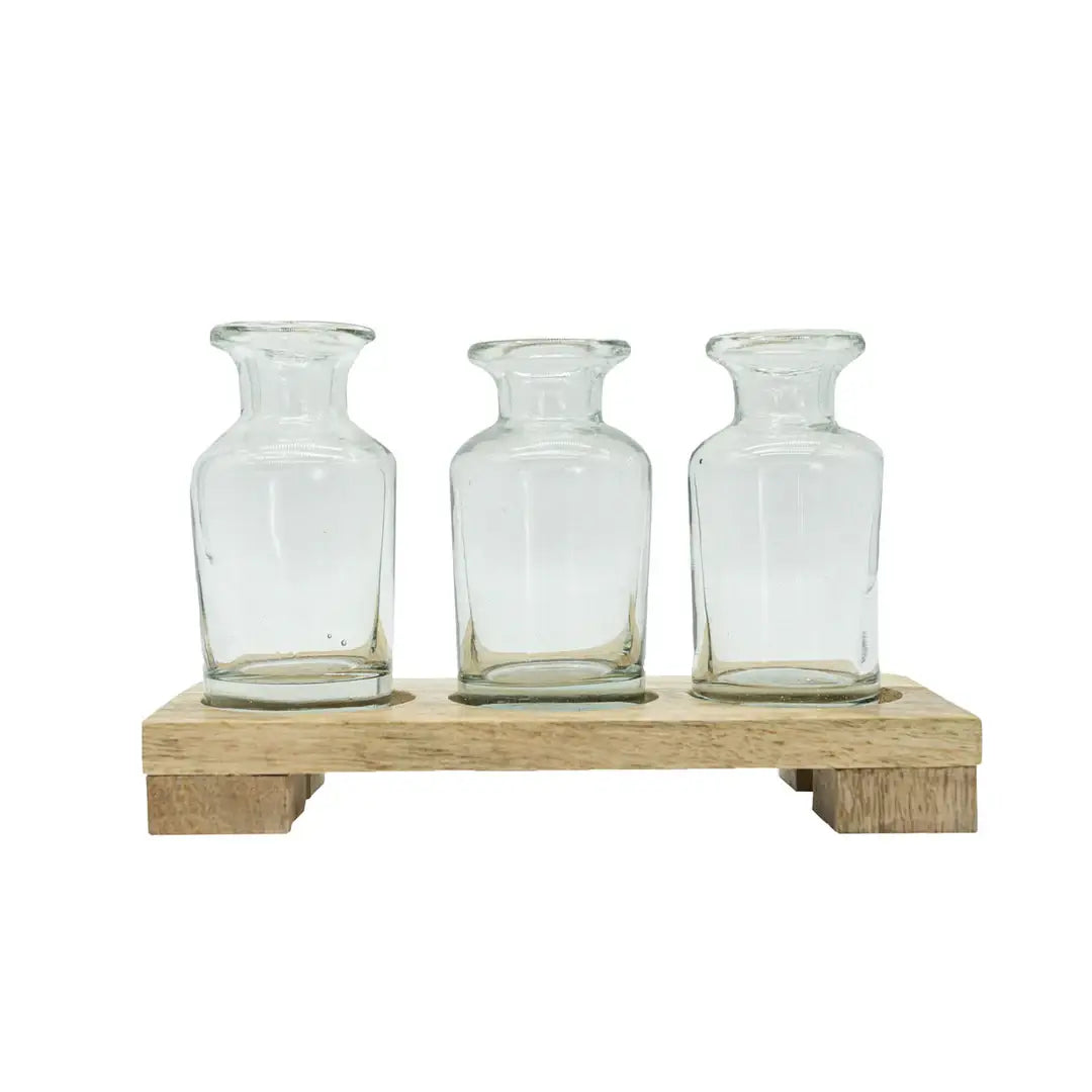 Three clear glass bottles on a wooden stand against a white background