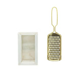 Gold grater next to a white rectangular container on a white background