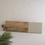 Wooden cutting board with a beige end on a white surface with a plant in the corner