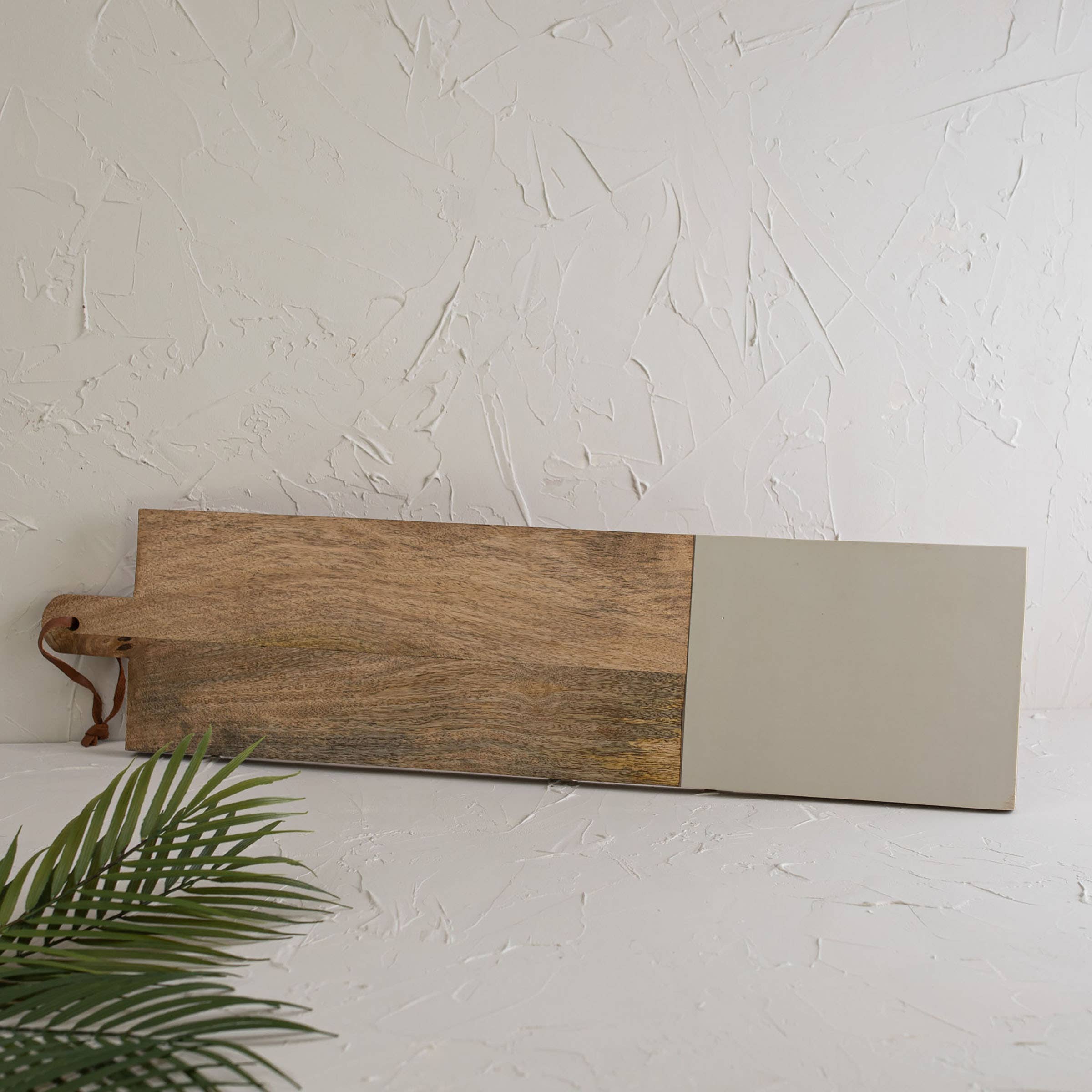 Wooden cutting board with a beige end on a white surface with a plant in the corner