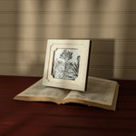 Open book with a framed picture of a tree on a wooden surface