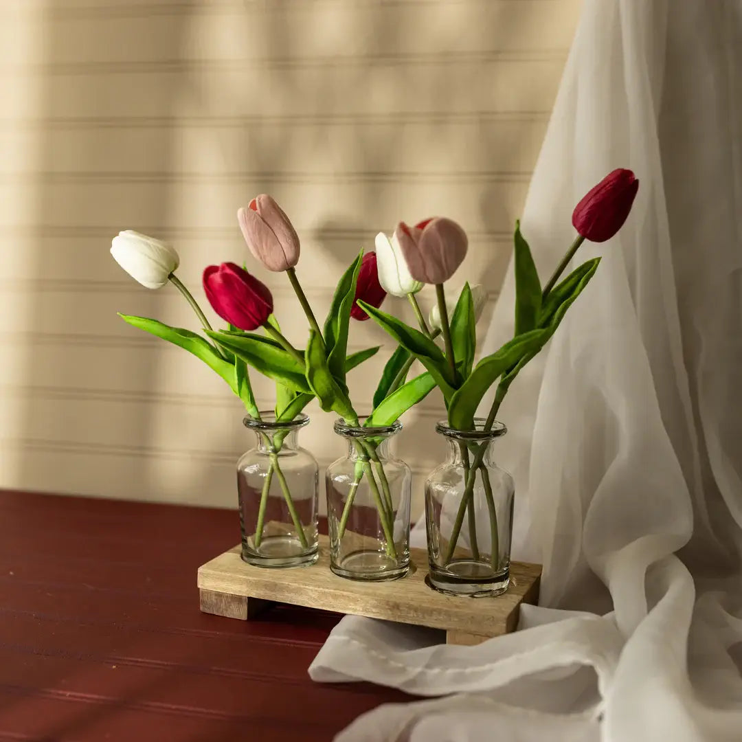 Four glass vases with tulips on a wooden stand against a neutral background