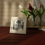 Framed artwork on a wooden surface with tulips in the background