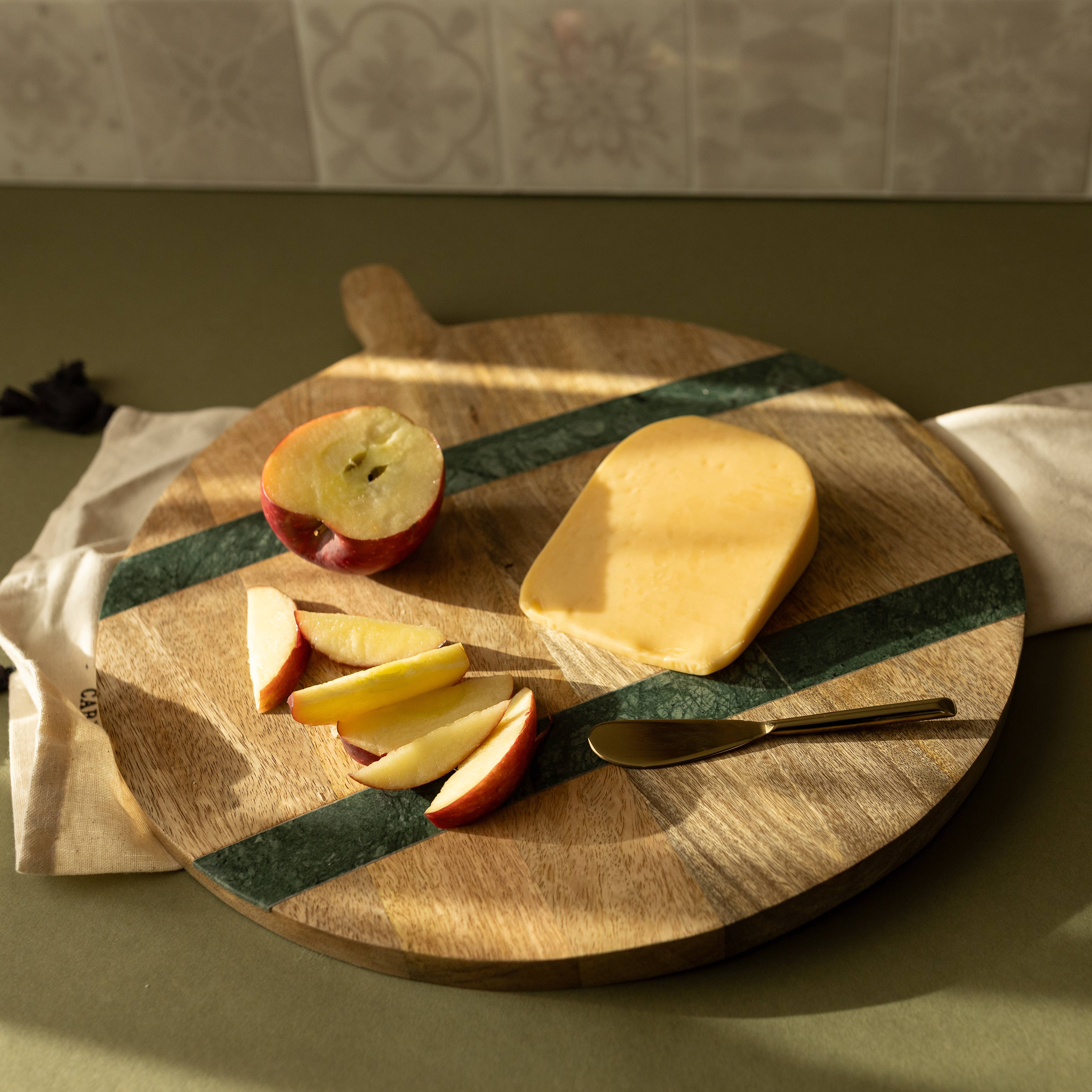 Wooden cutting board with sliced apples and a piece of cheese on a kitchen counter.