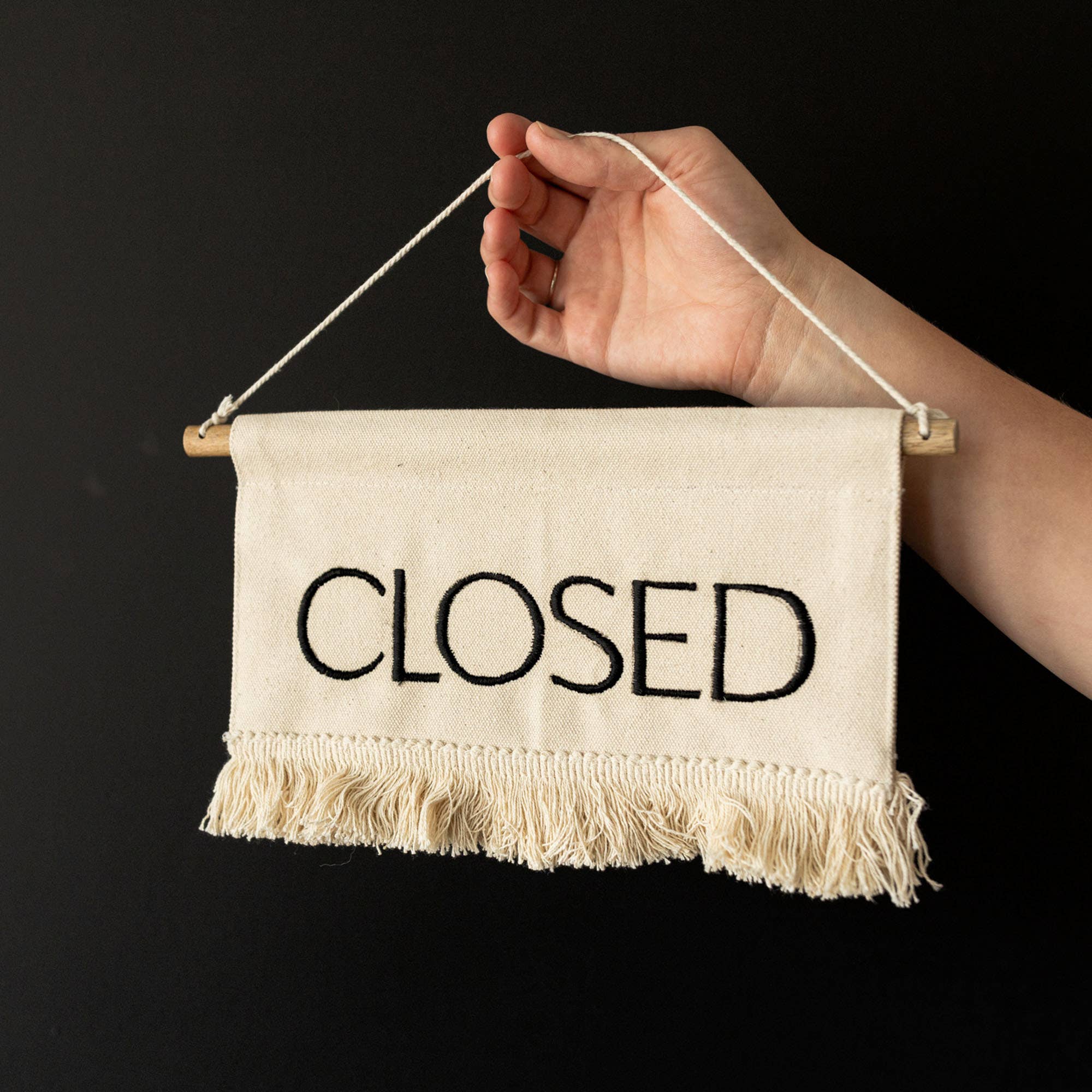 Hand holding a 'CLOSED' sign against a black background