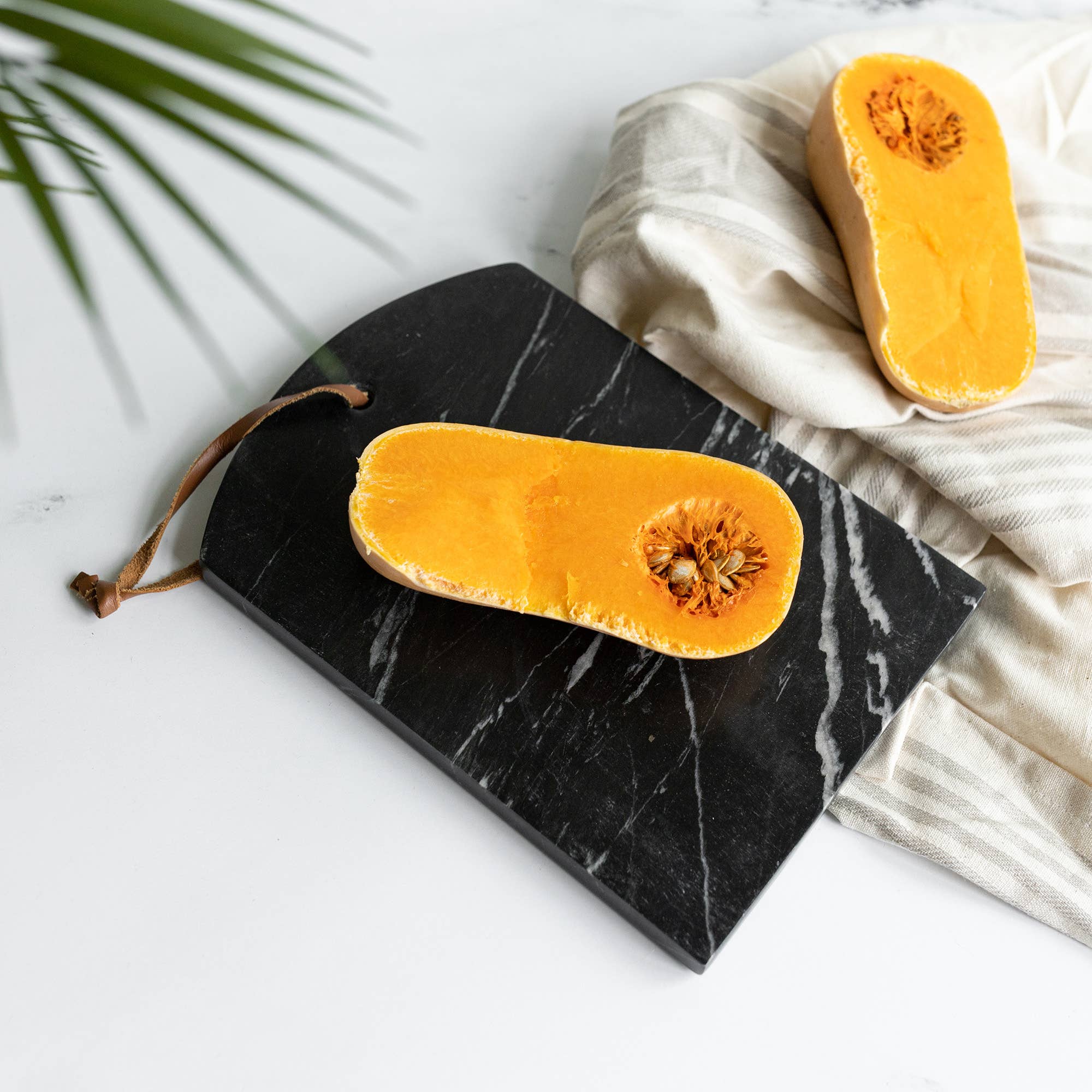 Sliced butternut squash on a black marble cutting board with a white cloth and green leaf background.