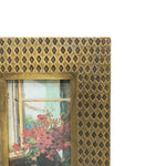 Decorative gold frame with a painting of flowers and a window.