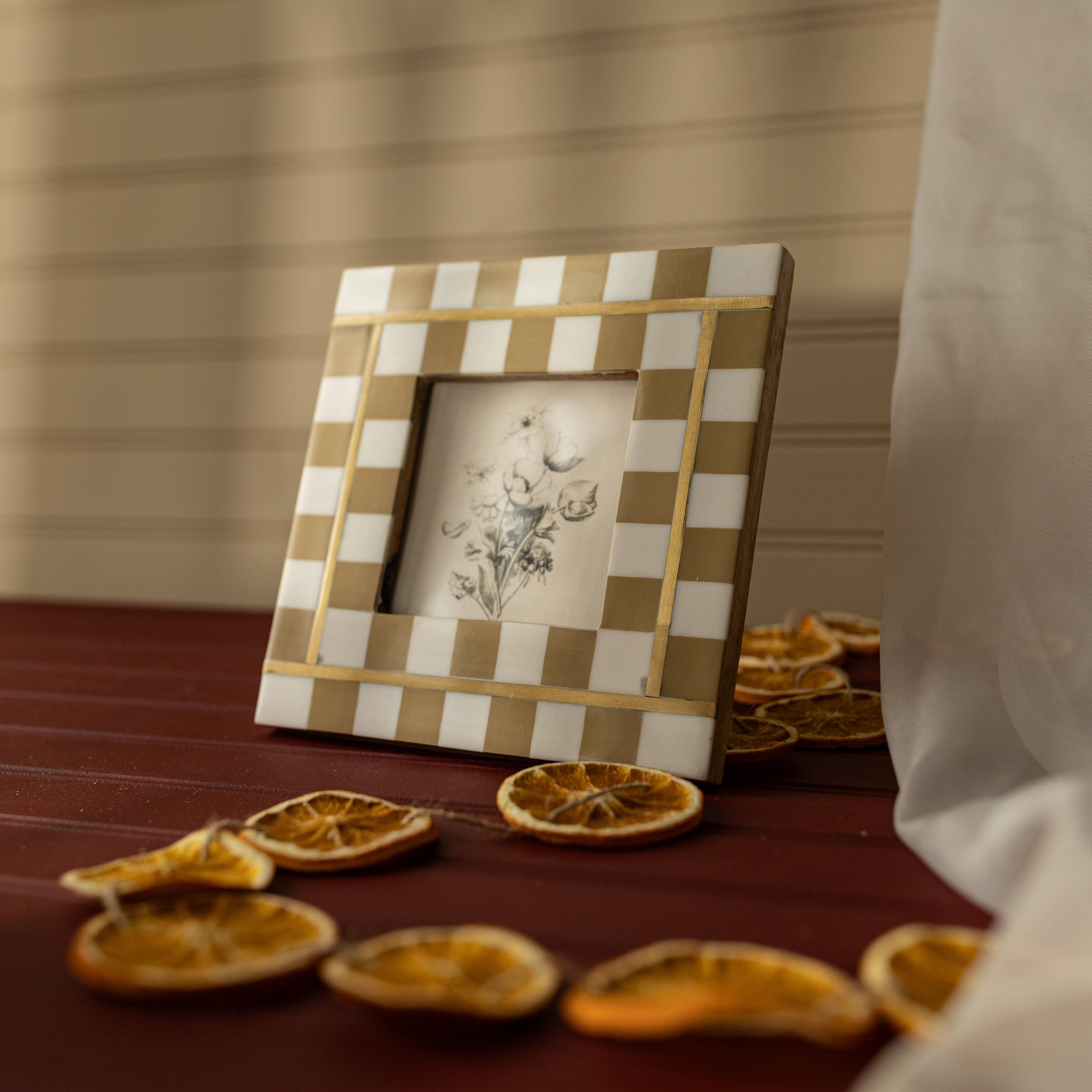 Decorative checkered frame with a small picture on a table with dried oranges.