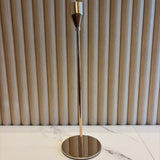 Gold Taper Candle Holder with metallic finish on a marble wall.