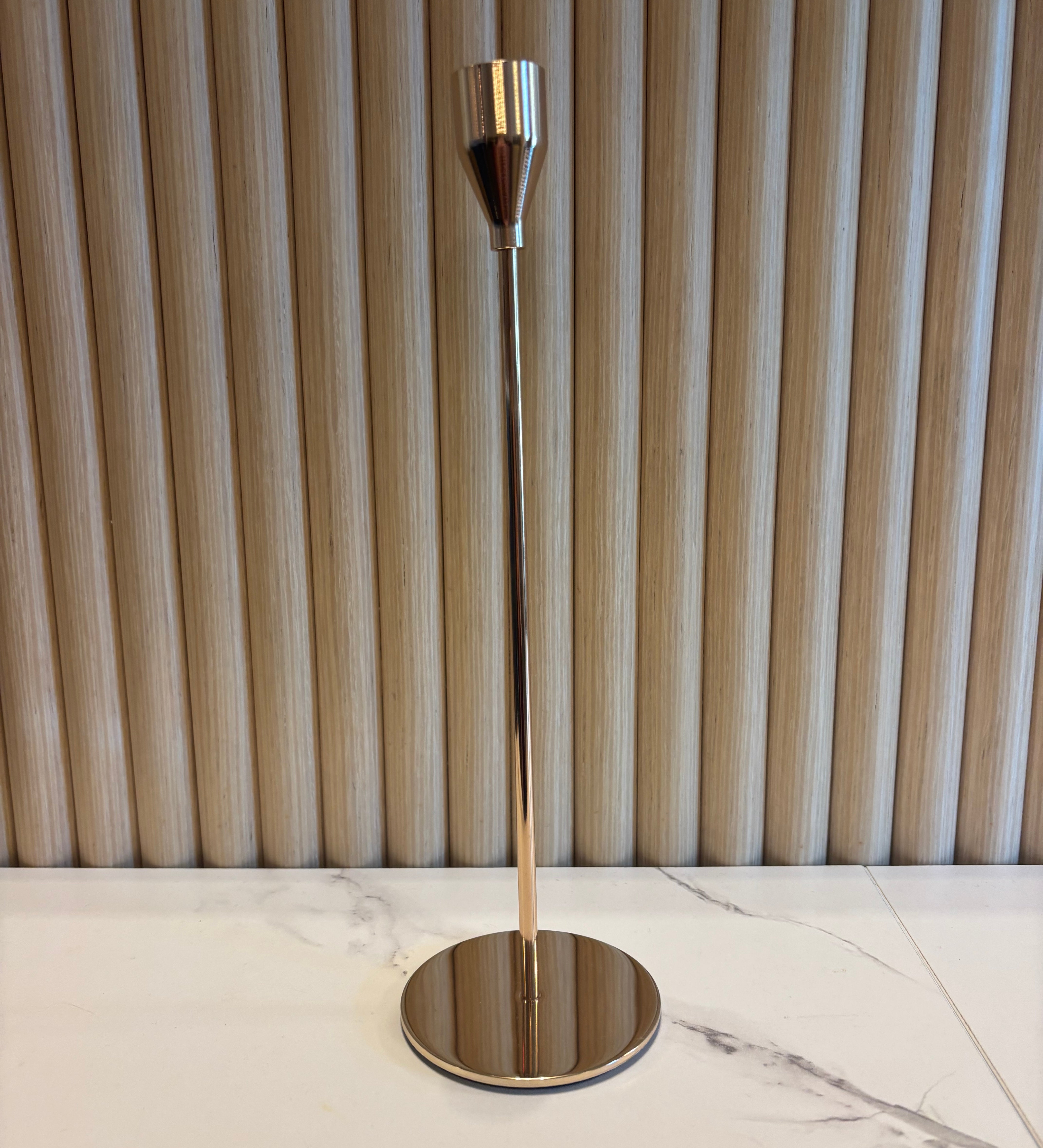 Gold Taper Candle Holder with metallic finish on a marble wall.