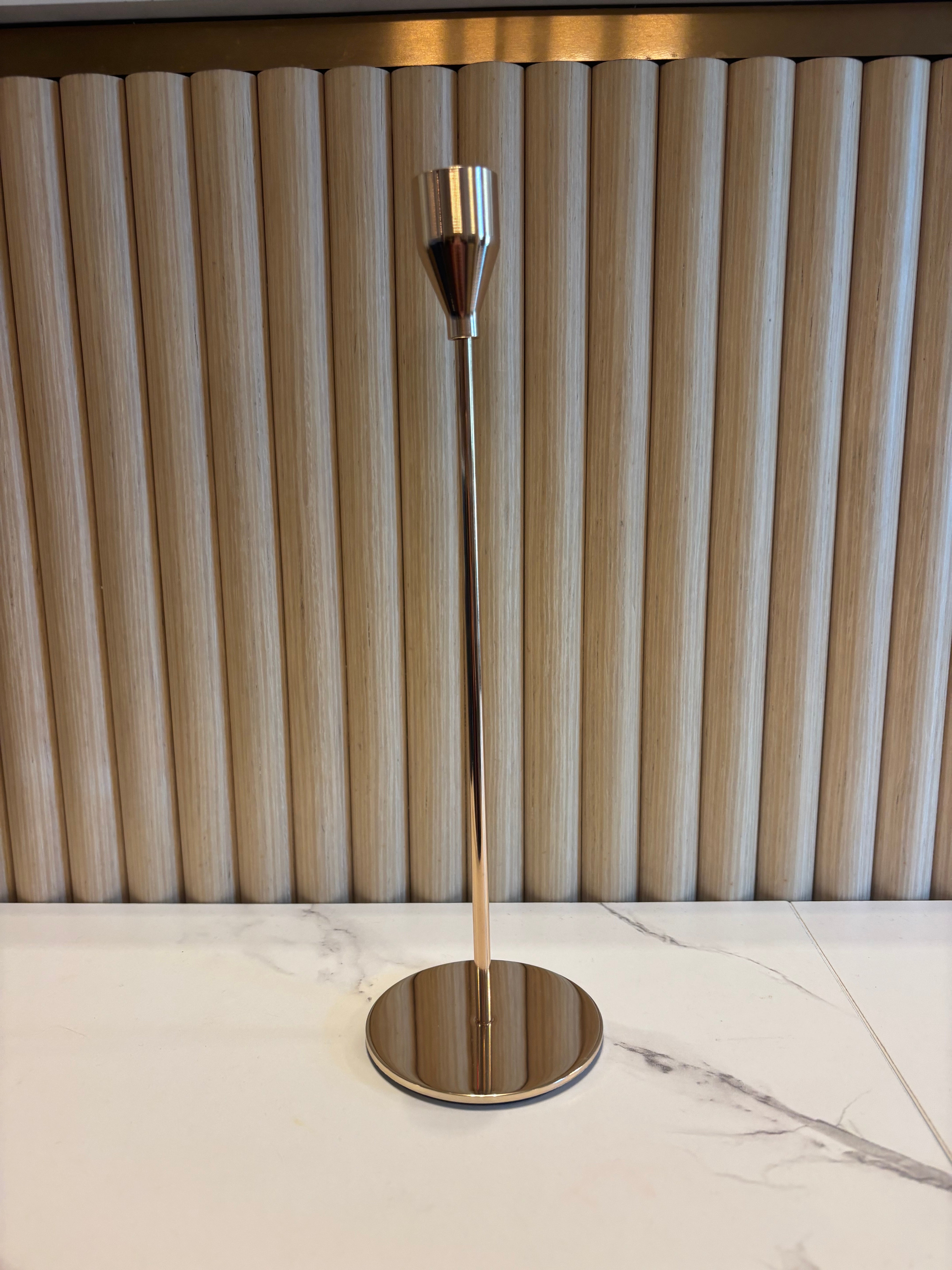 Gold Taper Candle Holder with metallic finish on a marble wall.