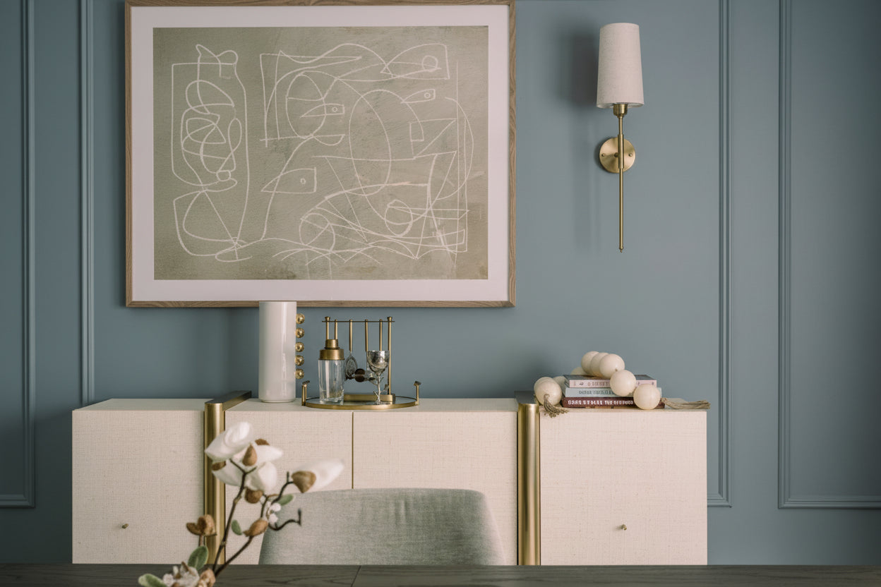 Modern interior with abstract art, wall sconce, and decorative items on a cabinet.