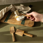 Wooden cheese knives on a cutting board with a block of cheese.