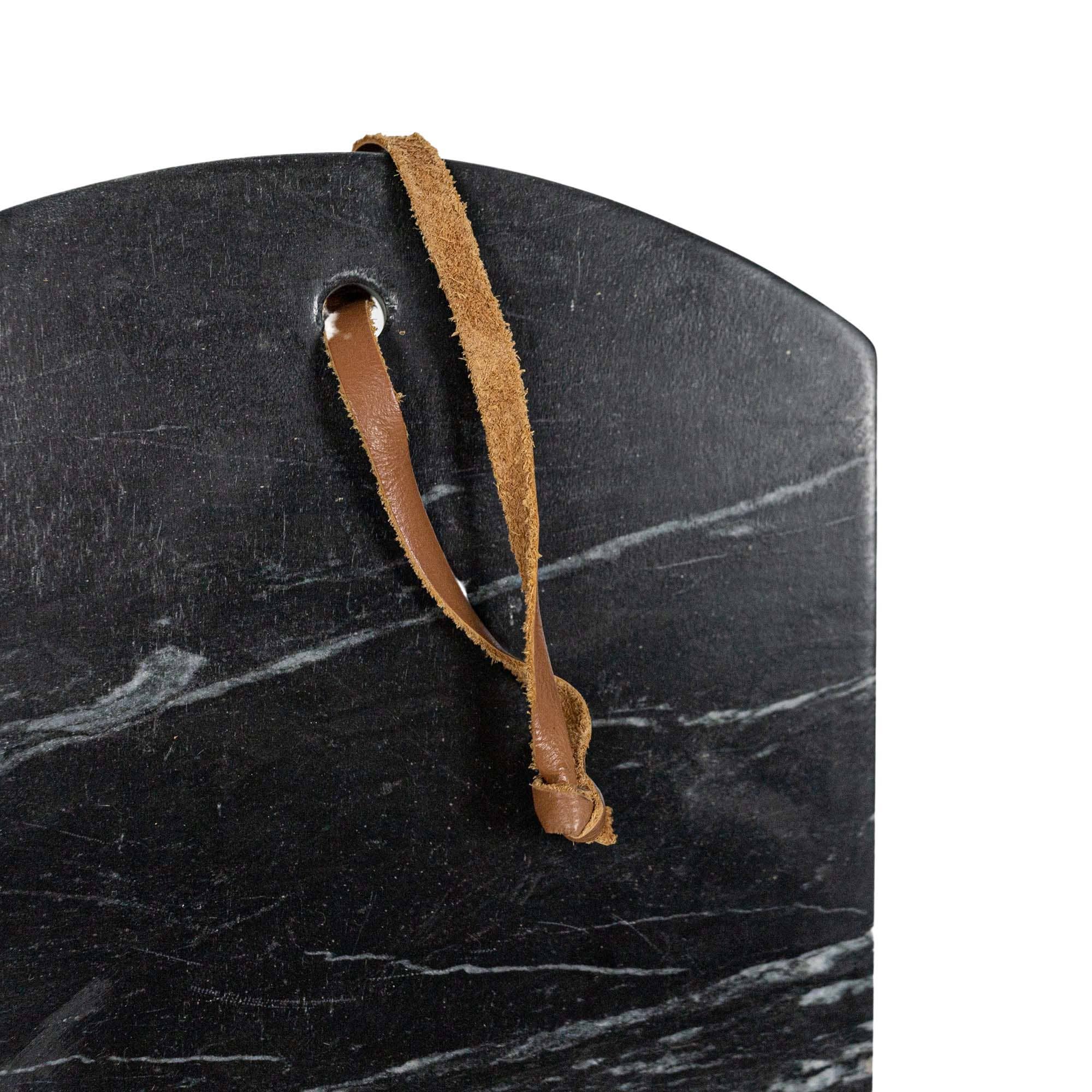 Black marble cutting board with a brown leather handle on a white background