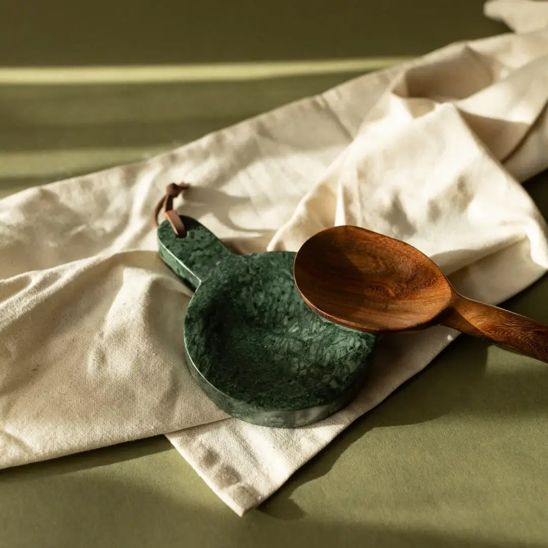 Green ceramic spoon rest and wooden spoon on a light fabric background