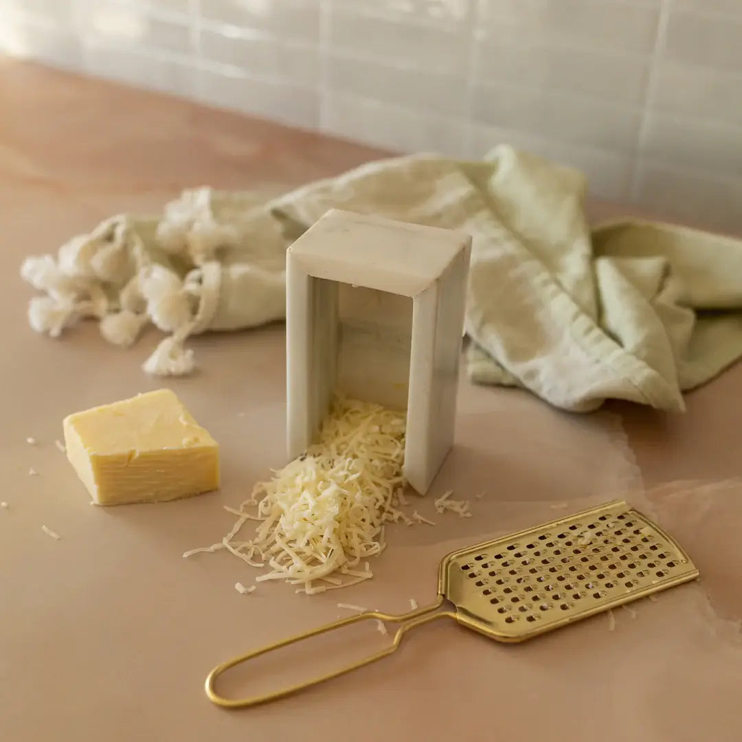 Cheese grater with grated cheese and a block of cheese on a wooden surface.