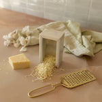 Cheese grater with grated cheese and a block of cheese on a wooden surface.