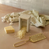 Cheese grater with grated cheese and a block of cheese on a wooden surface.