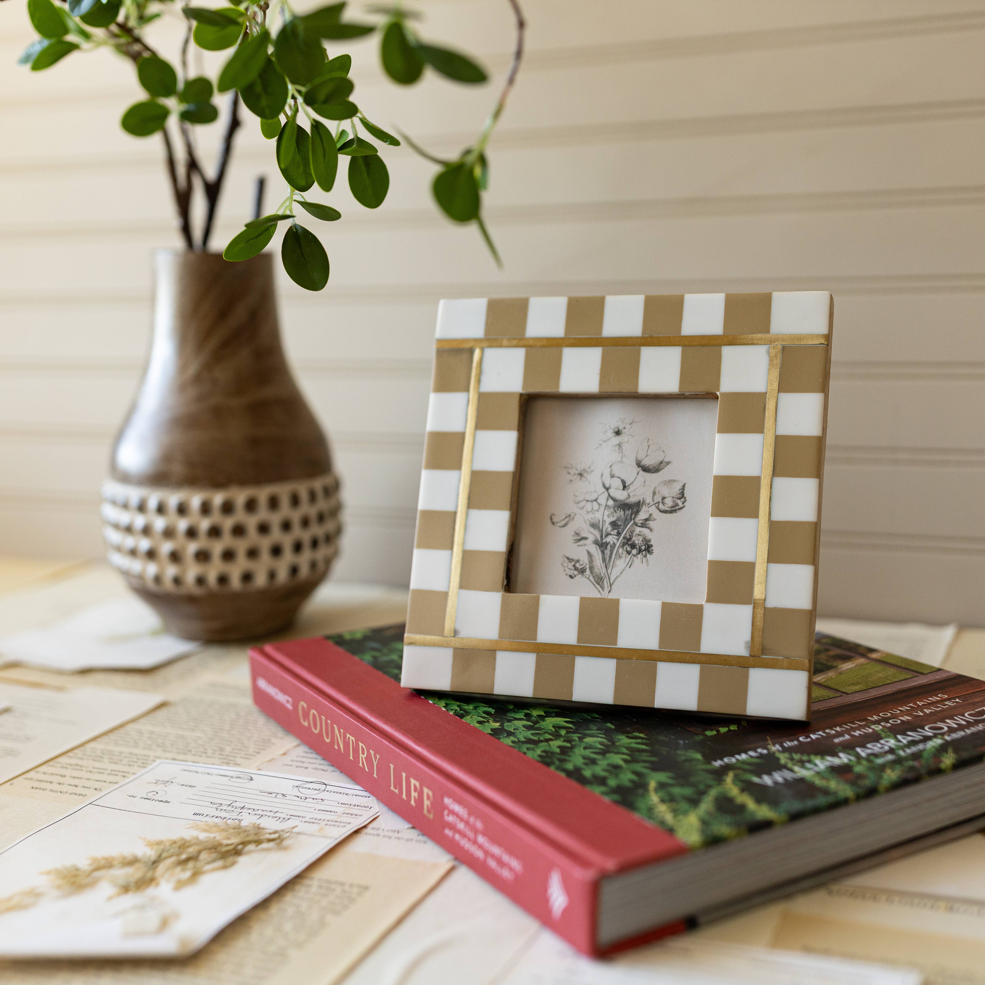 Checkered photo frame on a stack of books with a vase and plant in the background
