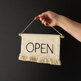 Hand holding a 'OPEN' sign against a black background