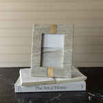 Marble and gold photo frame on top of a book titled 'The Art of Home'.