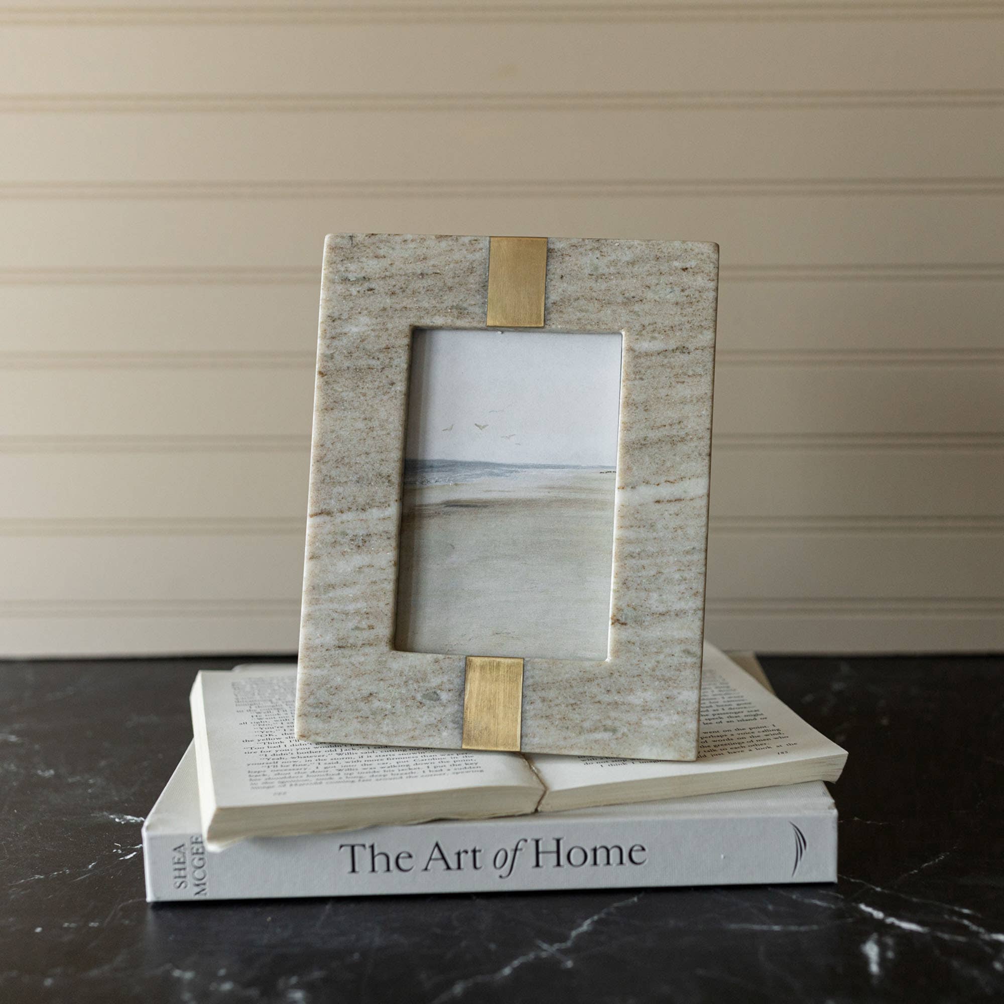 Marble and gold photo frame on top of a book titled 'The Art of Home'.
